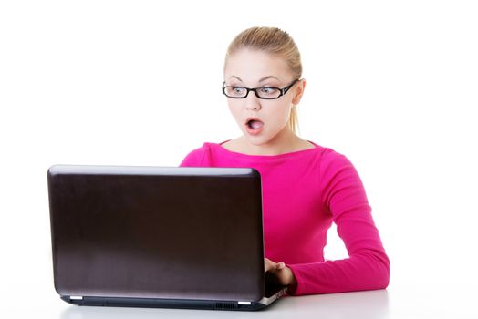 Young surprised woman sitting in front of laptop. Isolaed on white.