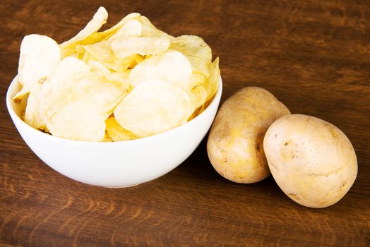 Potatoe chips in a bowl and potatoes. Over wooden background.