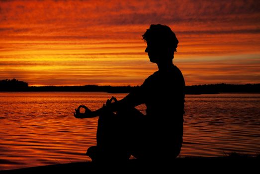 Silhouette woman sitting and relaxing against orange sunset 
