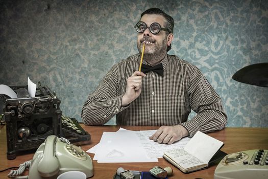 Pensive office employee with a pencil in his mouth looking up in the 1960s