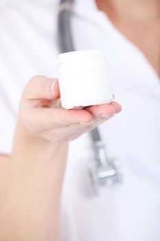 Young woman doctor nurse is holding white empty plastic bottle. Focus on the bottle.