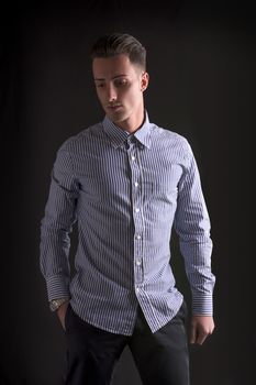 Smiling young man in striped shirt, looking down on dark background