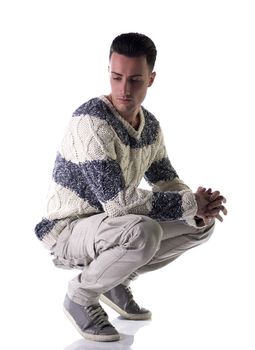 Good looking young man with winter sweater, sitting on his heels, isolated on white