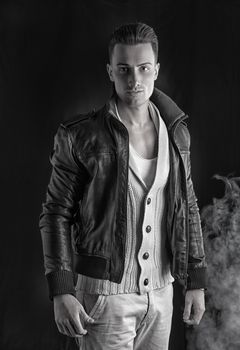 Attractive young man with white sweater and black leather jacket. Smoke and dark background