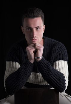 Good looking young man sitting, wearing winter sweater, on black background