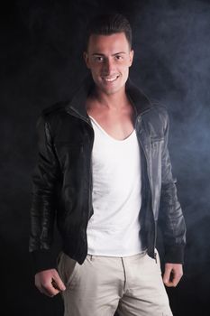 Smiling young man with white t-shirt and black leather jacket. Smoke and dark background