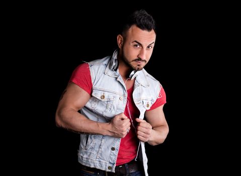 Musculare man with jeans gilet (vest) and headphones around his neck, on black background