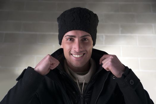 Smiling young man with wool hat and winter coat, indoors, looking at camera