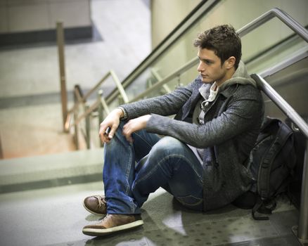 Handsome young man sitting on stairs' marble steps, backpack behind him
