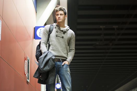 Handsome young man standing in train or subway station looking to a side, shot from below