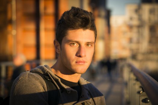 Handsome young man in city setting, lit by sunset light, looking at camera