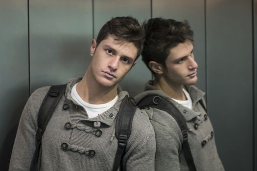 Handsome young man leaning against mirror inside an elevator (lift), looking at camera