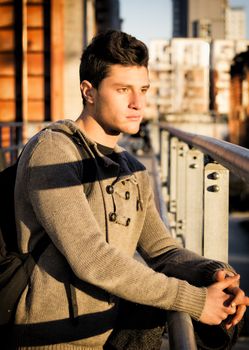 Handsome young man in city setting, lit by sunset light, looking away