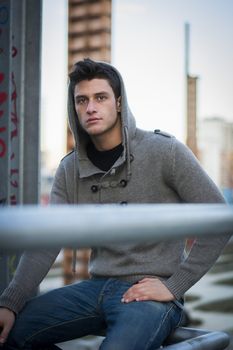 Handsome young man in industrial environment with wool hoodie and jeans, looking at camera