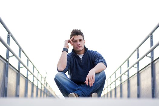 Handsome young man sitting between handrails in walkway, looking at camera