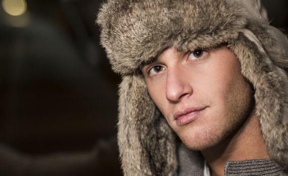 Headshot or handsome young man wearing fur hat, looking at camera