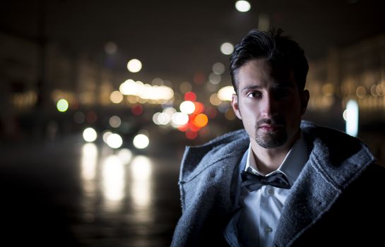 Attractive young man portrait at night with city lights behind him in Turin, Italy