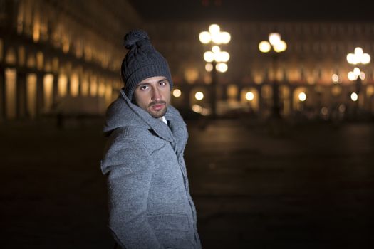 Attractive young man at night in Piazza Castello in Turin, Italy, wearing wool hat and coat