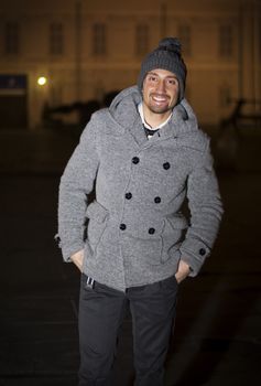 Attractive young man at night in Piazza Castello in Turin, Italy, wearing wool hat and coat
