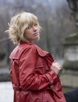 Attractive young woman with red leather jacket, seen from a side. Outdoors shot
