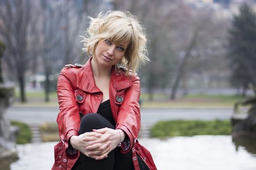 Attractive young woman with red leather jacket sitting in a park