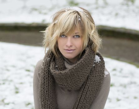 Attractive blonde young woman with wool scarf, snow around her