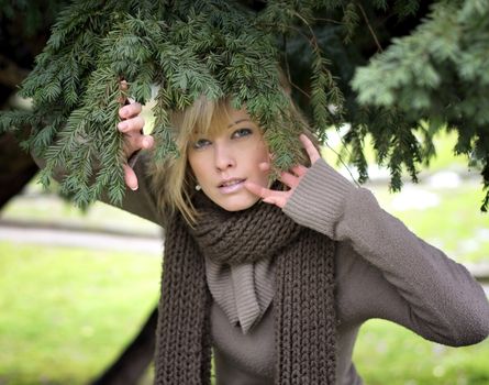 Attractive blonde young woman in park, winter time, under a pine tree