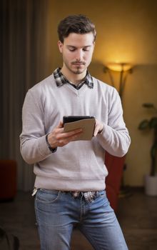 Handsome young man at home in his living room using tablet PC