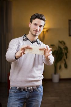 Handsome young man holding check in his hands, smiling and looking at camera