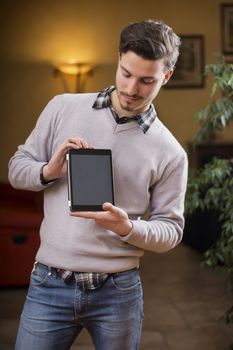 Handsome young man at home in his living room showing tablet PC's screen