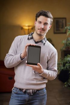 Handsome young man at home in his living room showing tablet PC's screen