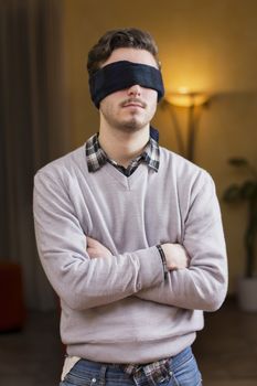 Blindfolded young man at home in living room cannot see