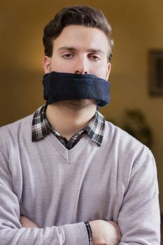 Young man with gag (scarf) on his mouth cannot speak
