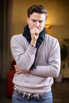 Young man at home sick, coughing, with hand in front of his mouth