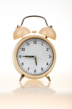 classic alarm clock on white table with reflection