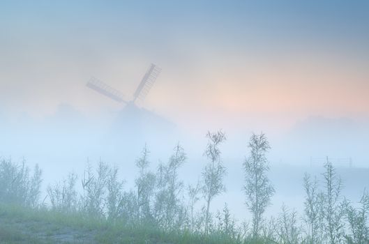 Dutch windmill in dense sunrise fog, Holland