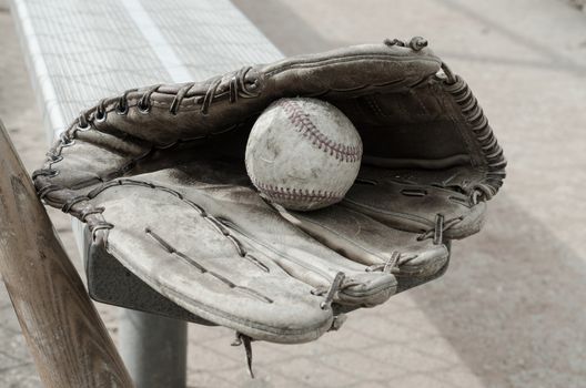 Baseball times gone by with ball and glove on bench in dugout with bat.