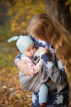 Mother walking with child outdoor, baby nursing in sling