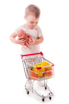 Little girl plays with shopping trolley and doll. Grocery store playing