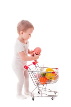 Little girl plays with shopping trolley and doll. Grocery store playing