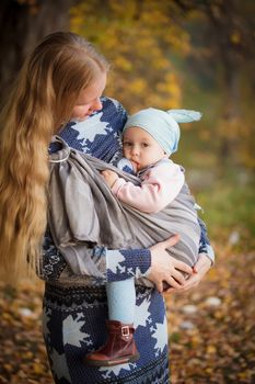 Mother walking with child outdoor, baby nursing in sling