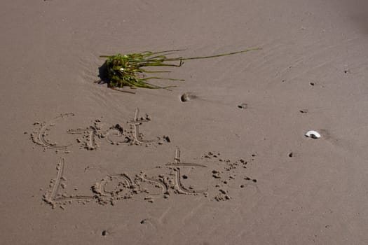 The words "get lost" written in the sand of a beach showing a vacation or getaway that is relaxing.