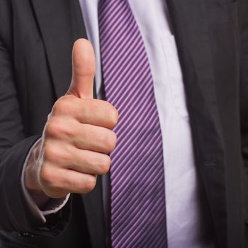 Detail shot of a businessman in suit gesturing thumbs up