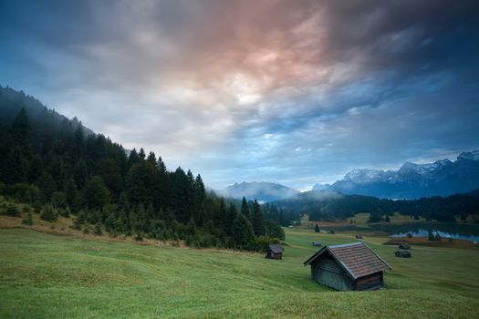 misty sunrise over huts by Geroldsee lake in Bavarian Alps, Germany