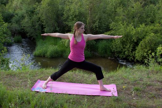 A pretty young woman doing Yoga poses in front of a forest stream.