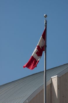 A Canadian flag in the breeze against a blue sky.