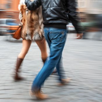 Man in jeans and a woman in a fur coat walking down the street hugging. Intentional motion blur