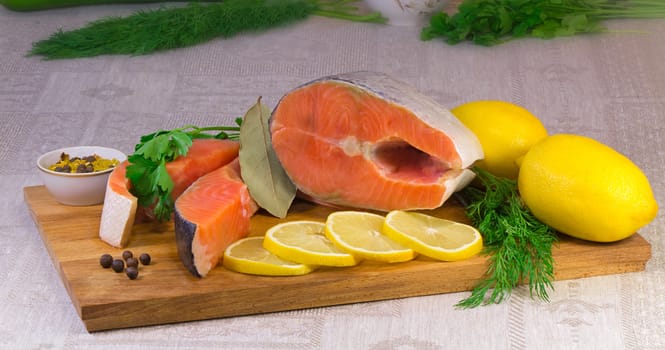 On the table are cut into large pieces of fish salmon, lemon, dill and parsley, spices for cooking fish.