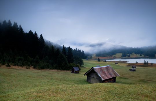 wooden huts and fog over Geroldsee lake in dusk, Bavarian Alps