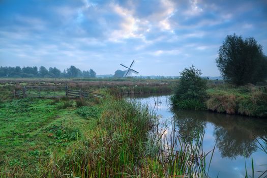 Dutch windmill and blue morning sky reflected in river